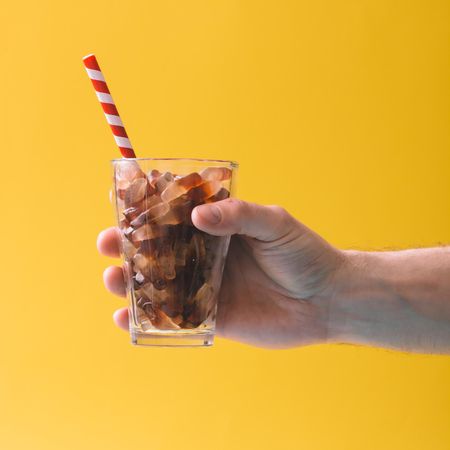 Glass full of gummy candies with straw on yellow background