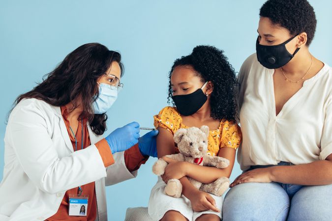 Small girl holding her teddybear getting covid-19 vaccine from a pediatrician