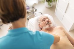 An older man, lying on the table in a physiotherapy clinic, during a therapy session with his physio