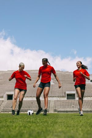 Three females playing football during team practice in field