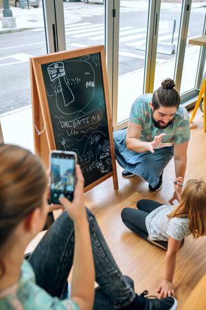 Family business owners taking a break playing with daughter and taking photos in cafe restaurant