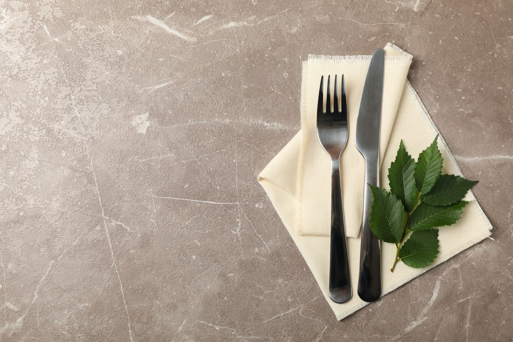 Napkin, cutlery and leaves on gray background, space for text
