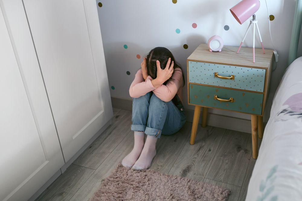 Unrecognizable girl with mental disorder holding head with hands sitting on the floor
