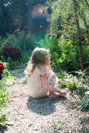 Side view of little girl sitting on pebble path in garden