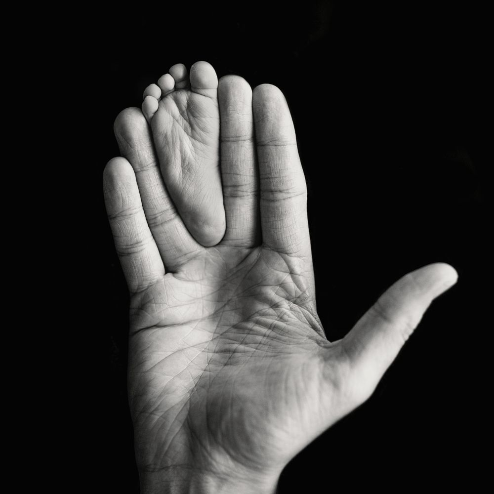 Grayscale photo of hand holding baby foot