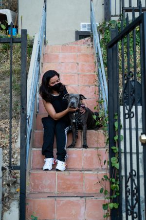Woman in athletic attire sits with her dog on steps before a dog walk