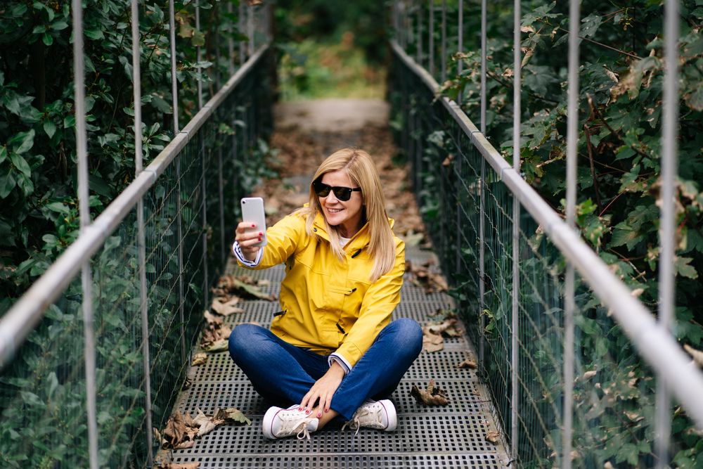 Happy female traveler taking selfie on suspension bridge in summer
