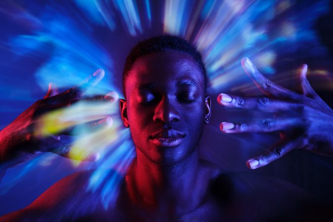 Shirtless Black man holding hands near face in blurred lights
