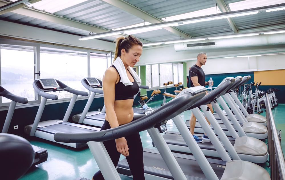 Fit male and female warming up on treadmills in gym