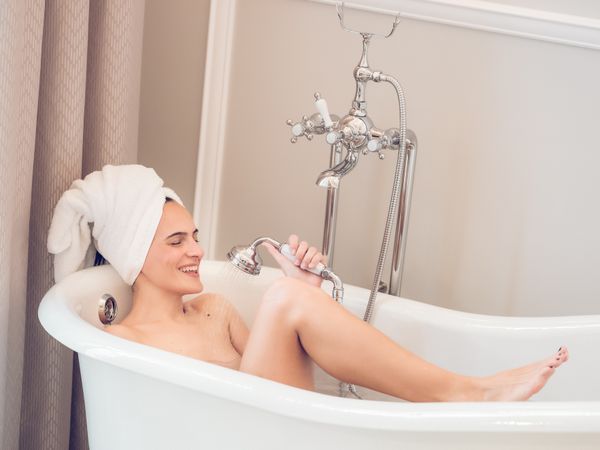 Smiling woman resting in bathtub and washing with shower