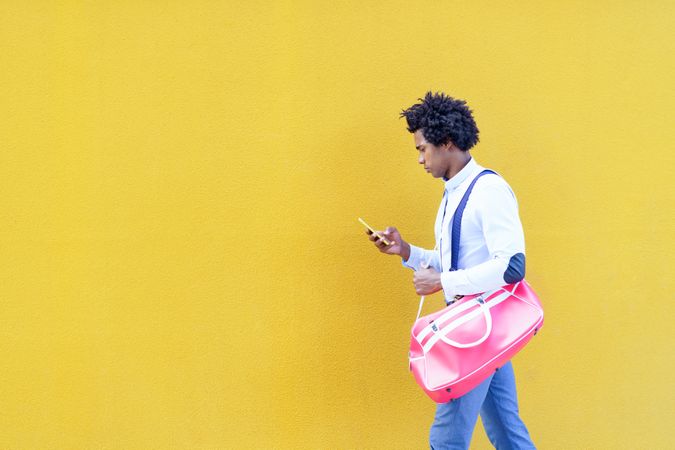 Man with bright pink back checking phone walking next to yellow wall