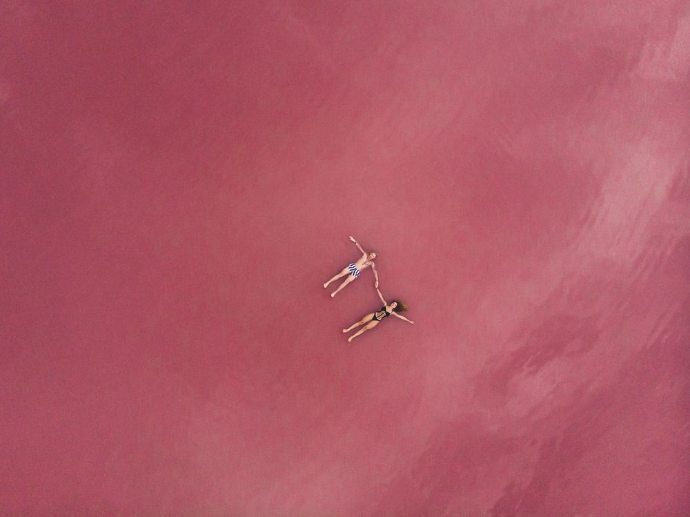 Idyllic couple in swimwear floating in pink water of lake