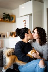 Loving female couple kissing on sofa with pet dog