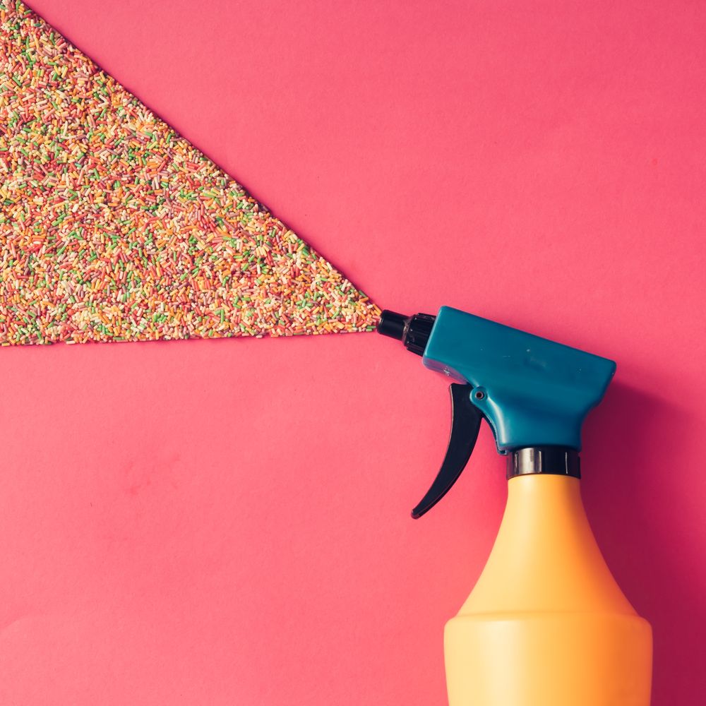 Spray bottle spraying sprinkles on pink background