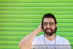Smiling man in sunglasses listening to headphones in front of green background 4ByZd5