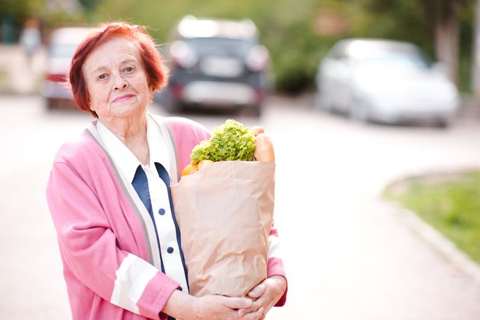 Older woman holding grocery bag standing on street