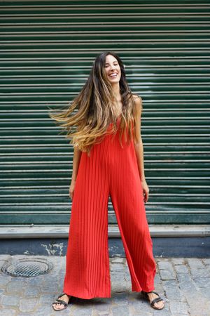 A woman in a vibrant red jumpsuit poses confidently against a green background, radiating energy