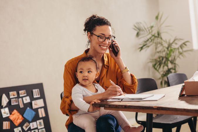 Working mother making notes while talking on mobile phone
