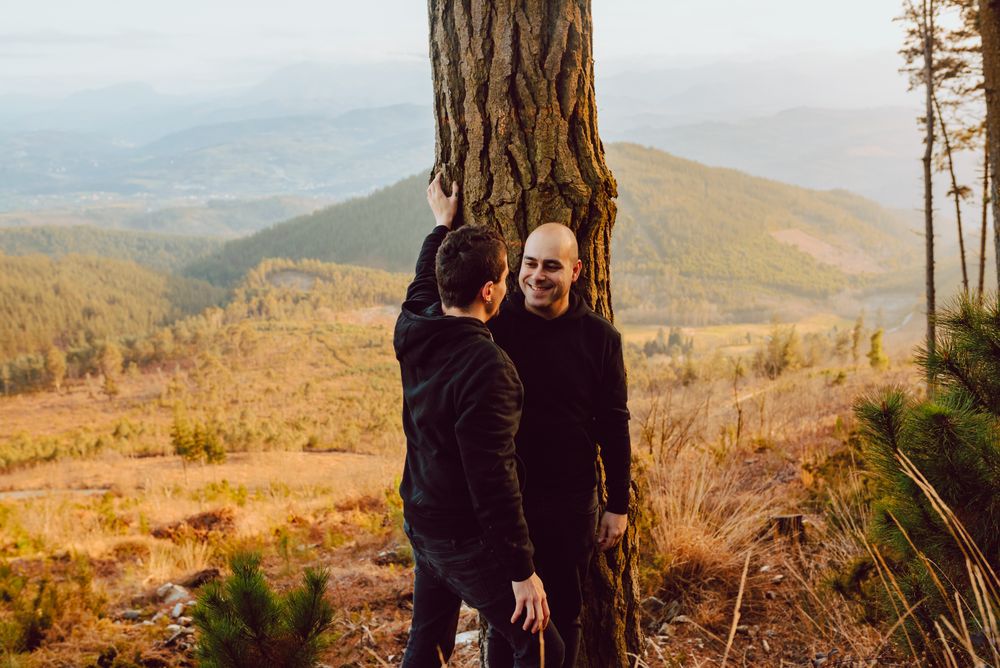 Smiling men hugging near tree in forest on hill