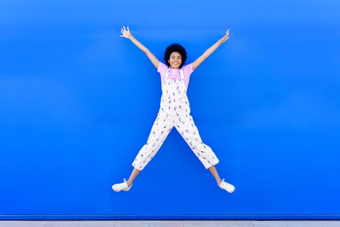 Woman in coveralls jumping in front of blue wall