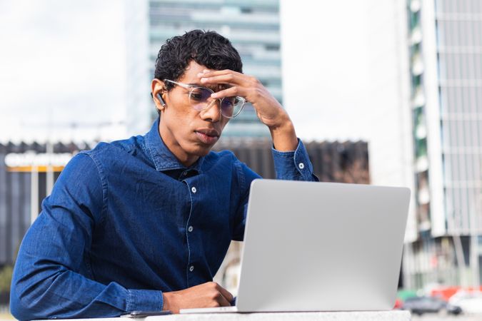 Serious male freelancer watching laptop in city