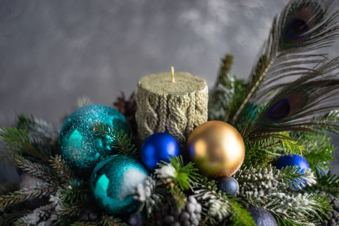 Blue and gold Christmas decorations in pine centerpiece with candle and peacock feathers