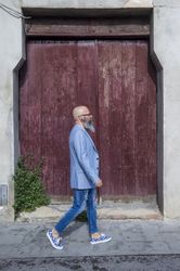Side view of a mature trendy bearded hipster walking against a red vintage door outdoors