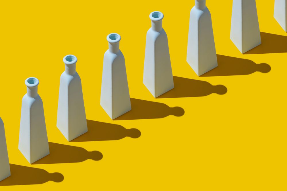 Single row of painted glass bottles and shadows on yellow background
