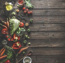 Food background with organic vegetables, healthy ingredients and kitchen utensils on dark rustic wooden table. Top view. Copy space.