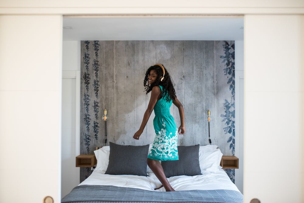 Black girl with headphones dancing on bed