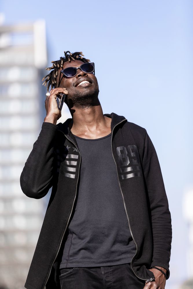 Black smiling man with sunglasses using mobile phone outdoors