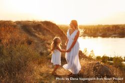 Female child in dress dancing with woman by river at dusk 0yZWj5