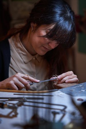 Attentive craftswoman using flat file while creating jewe
