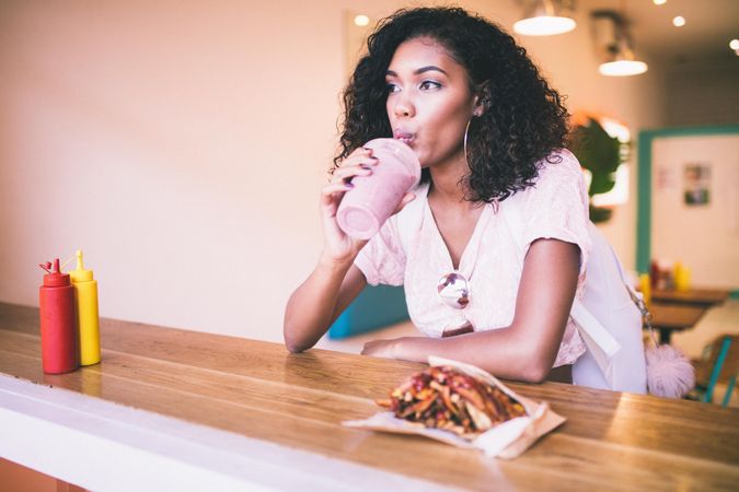 Young woman drinking a shake with fries on the side