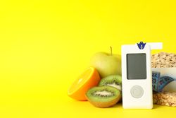 Blood glucose meter and diabetic food on yellow background