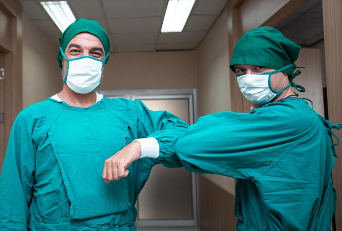 Two medical professionals in scrubs greeting each other with elbow bump