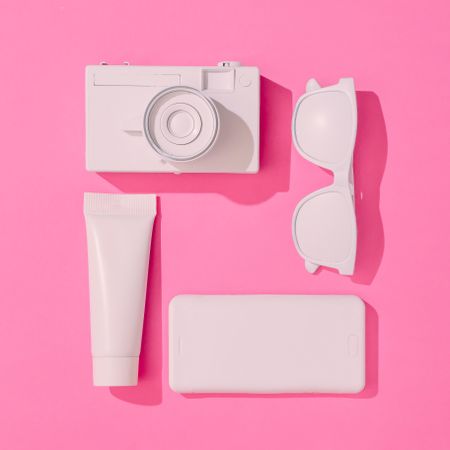 Summer objects of sunglasses, camera, smart phone and sunscreen on pink background