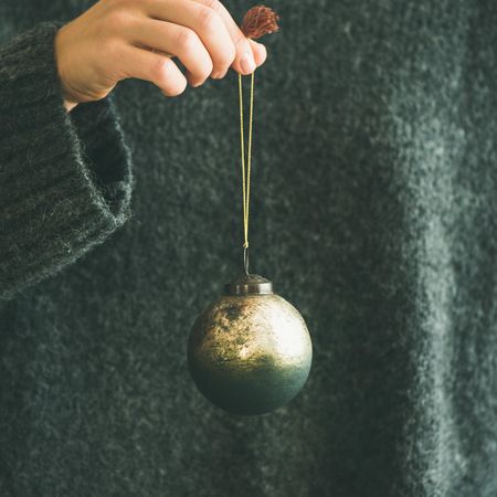 Woman holding single gold Christmas tree decoration, square crop