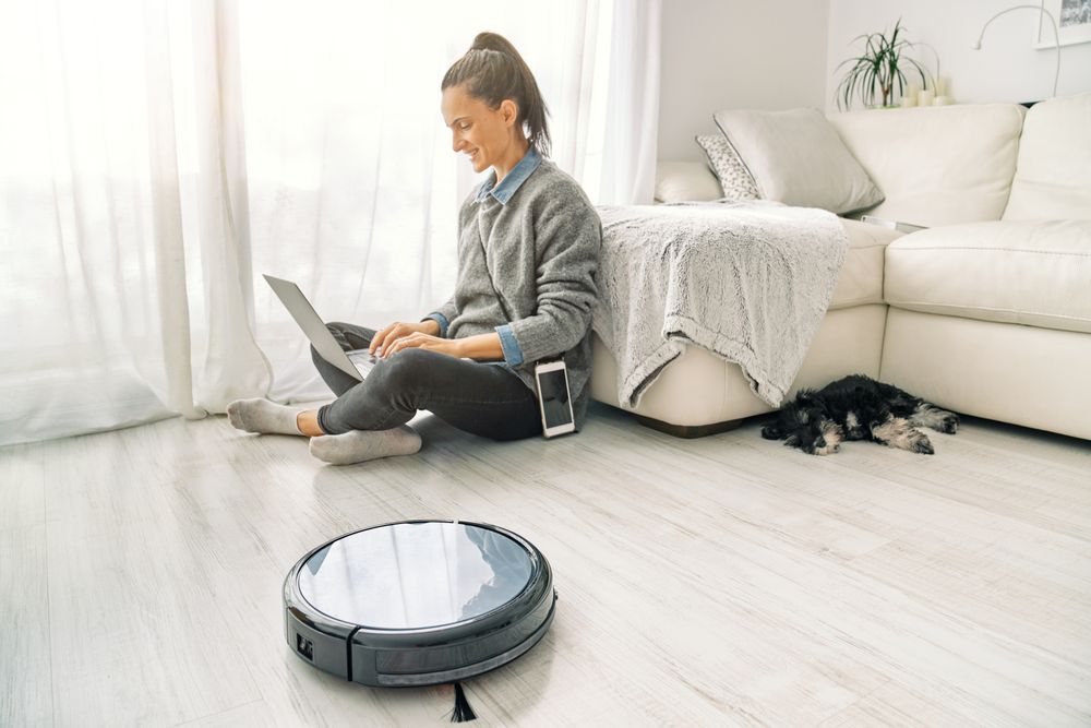 Female freelancer using laptop and sitting on floor near robotic