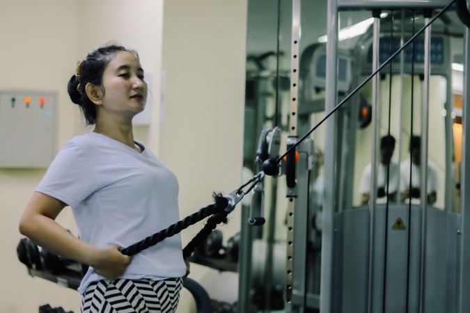 A woman indonesia is exercising on a cable machine at a fitness center
