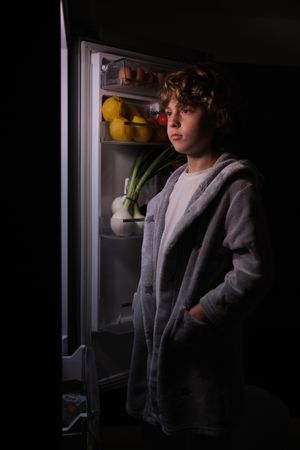 Calm boy in bathrobe near fridge at night time