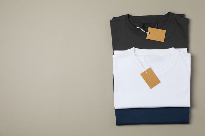 Folded blank t-shirts with tags on gray background, space for text