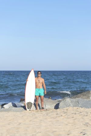 Male surfer standing with red outlined board on rocky seashore