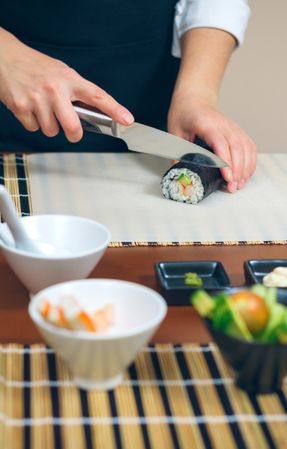 Female chef cutting Japanese sushi rolls with rice, avocado and shrimps in nori seaweed sheet