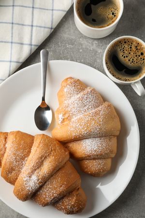 Plate with croissants, cups of coffee and towel on grey background, top view, vertical composition