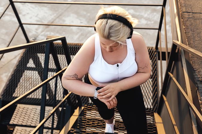 Curvy blond woman checking smart watch on outdoor staircase