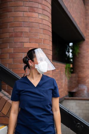 Portrait of woman nurse wearing blue scrubs, face shield and mask