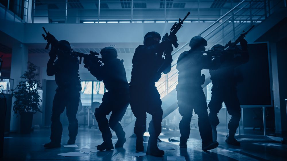 Masked Fireteam of Armed SWAT Police Officers Storm a Dark Seized Office Building with Desks and Computers.