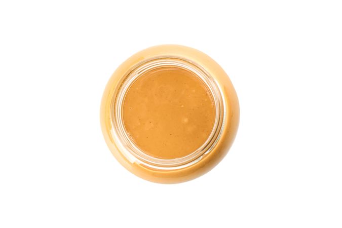 Creamy peanut butter in glass jar isolated on bright background, top view. A traditional product of American cuisine
