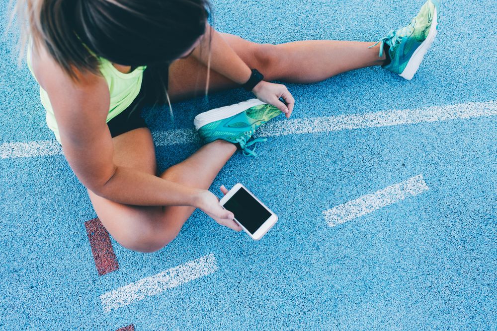 Woman stretching on a track field with phone